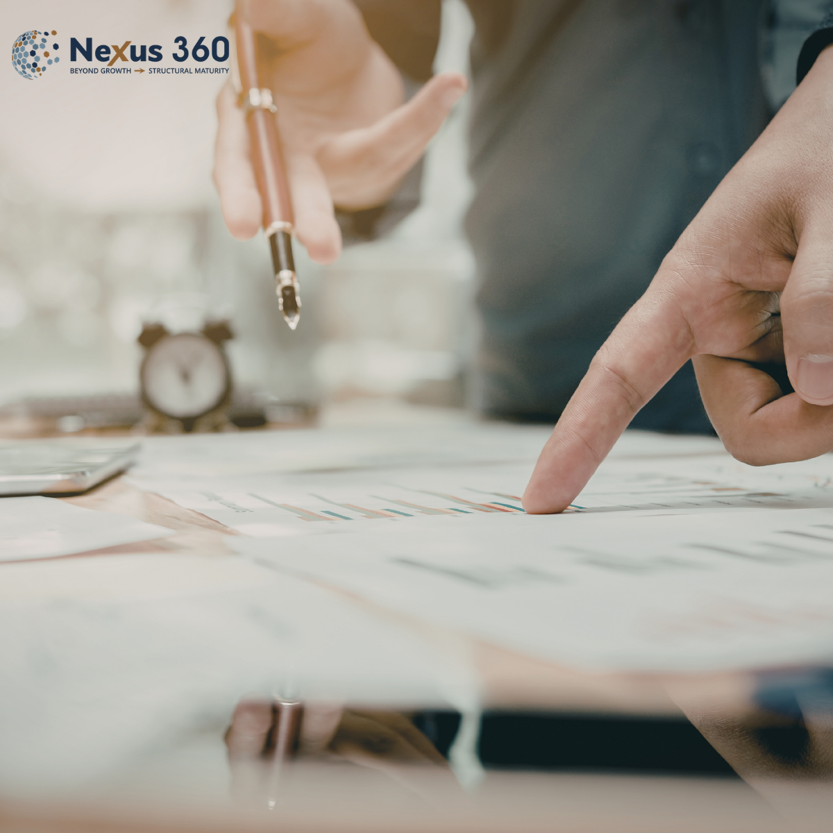 Picture of a person point with a finger and another pointing with a pen at bar charts on paper
