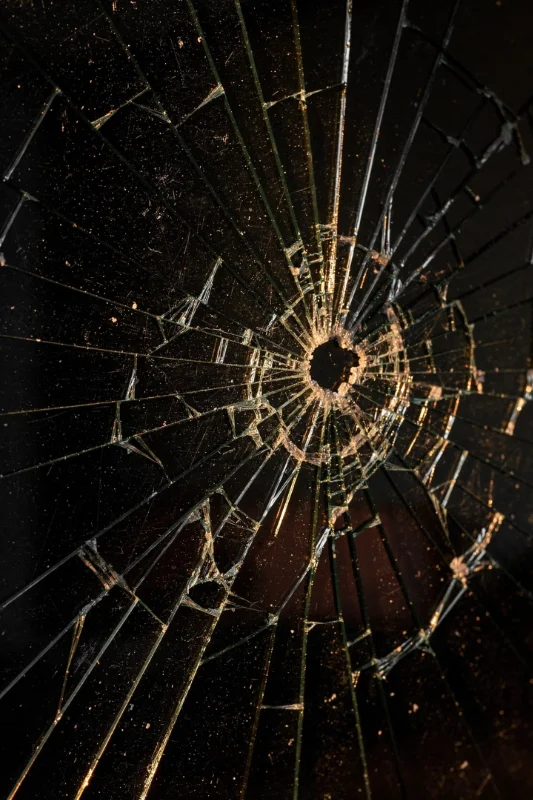 A broken pane of glass with a small hole in the middle and lots of cracked glass around it. 