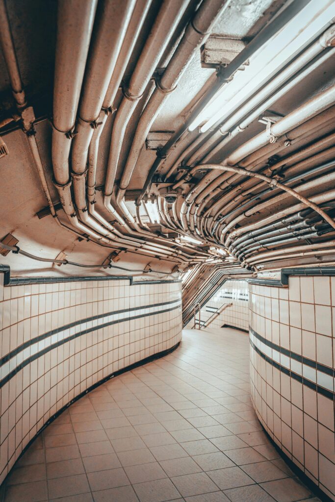 An entrance to an underground tube station which has lots of pipes layered across the ceiling